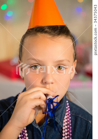 Girl blowing party horn during birthday party 34375043
