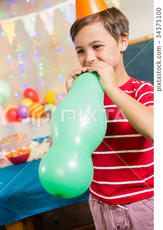 Cute boy blowing balloon during birthday party 34375100