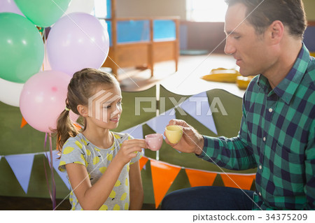 Father and girl toasting their tea cups while playing with toy kitchen set 34375209