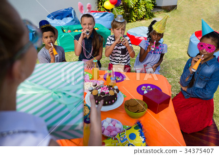 Girl holding gift while friends blowing party horn 34375407