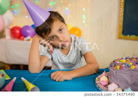 Boy sitting near a birthday cake at home Boy sitting near a birthday cake at home 34375490
