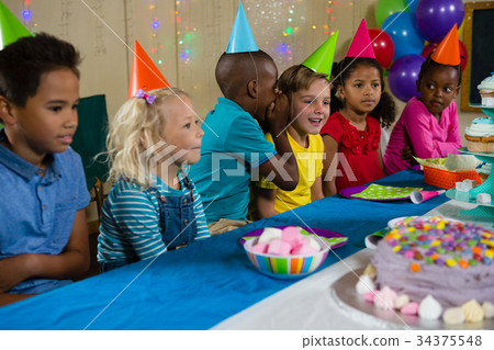 Boy whispering to girl while sitting with friends at table 34375548