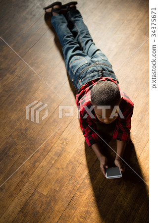 Boy lying on wooden floor using mobile phone 34375671