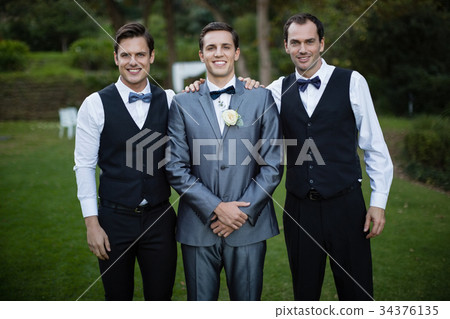 Smiling bridegroom and best man standing in garden Smiling bridegroom and best man standing in garden 34376135