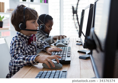 Side view of businessmen using computer while talking through headset at desk Side view of businessmen using computer while talking through headset at desk 34376374