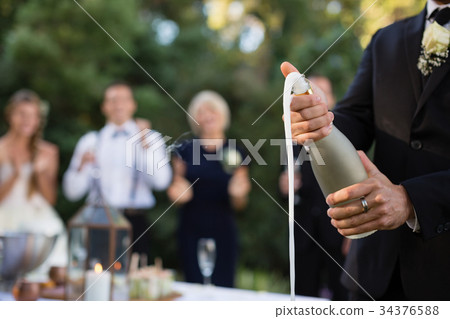 Groom opening champagne bottle at park Groom opening champagne bottle at park 34376588