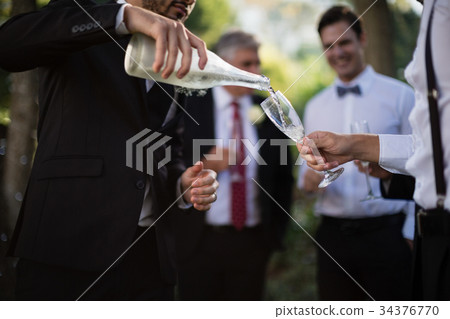 Groom pouring champagne into his friends glasses Groom pouring champagne into his friends glasses 34376770