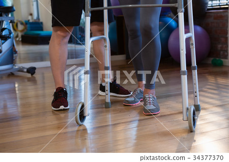 Physiotherapist helping patient to walk with walking frame in clinic 34377370