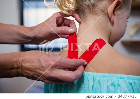 Physiotherapist sticking tape on girl patient 34377413