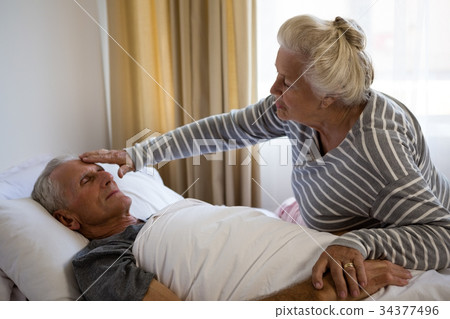 Senior woman sitting by husband sleeping on bed 34377496