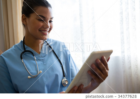 Smiling doctor using digital table in retirement home 34377628