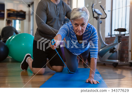 Physiotherapist assisting senior woman in performing exercise with resistance band 34377629