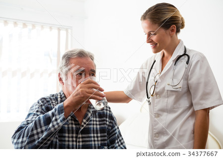 Female doctor standing by senior man drinking water 34377667