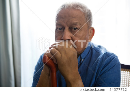 Portrait of sad senior man holding walking cane while sitting on chair Portrait of sad senior man holding walking cane while sitting on chair 34377712