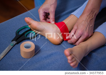 Physiotherapist sticking tape on girl patient 34377953