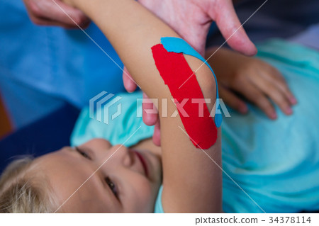 Physiotherapist sticking tape on girl patient 34378114