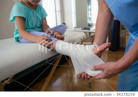 Physiotherapist putting bandage on injured feet of girl patient 34378159
