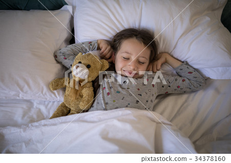 Girl sleeping on bed with teddy bear in bedroom 34378160