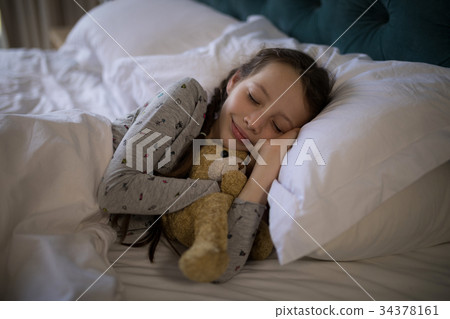 Girl sleeping on bed with teddy bear in bedroom 34378161