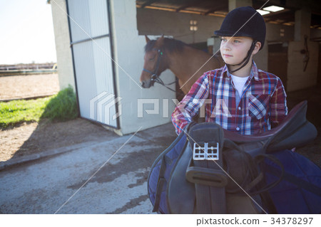 Teenage girl holding horse equipments in the stable 34378297