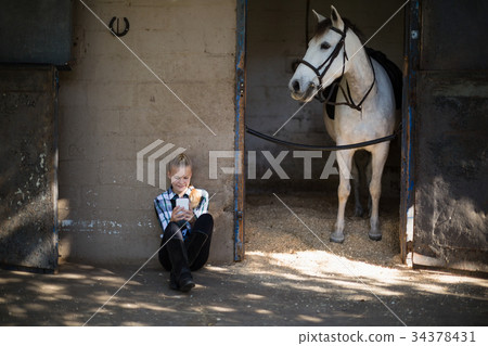 Teenage girl using mobile phone in the stable 34378431