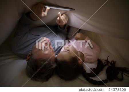 Father and daughter using digital tablet under blanket on bed 34378806