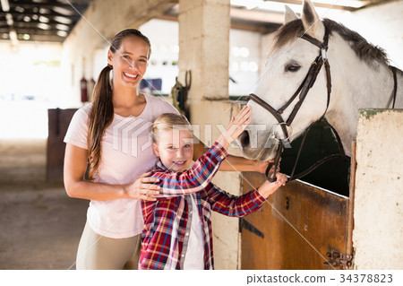 Portrait of sisters stroking horse 34378823