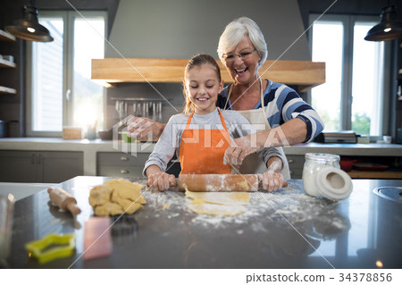Grandmother helping granddaughter to flatten dough 34378856