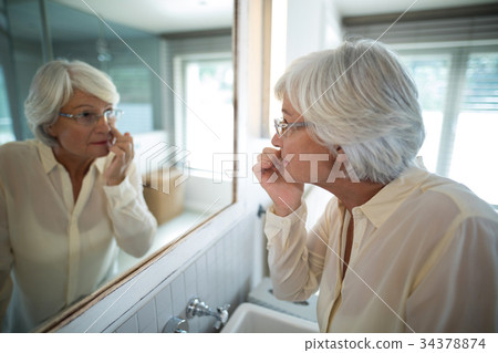 Senior woman checking her skin in mirror Senior woman checking her skin in mirror 34378874