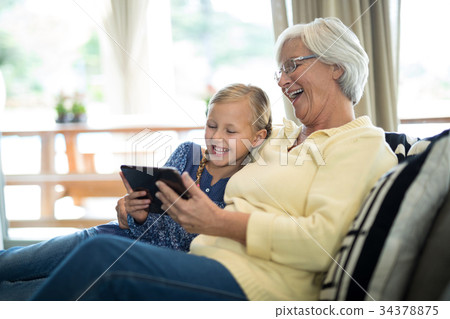 Smiling granddaughter and grandmother using digital tablet on sofa 34378875