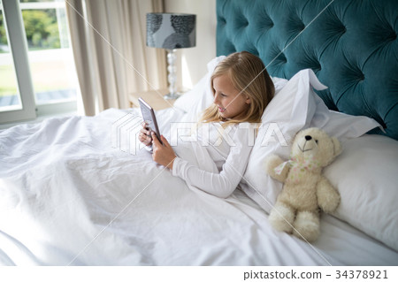 Girl using digital tablet while lying on bed 34378921
