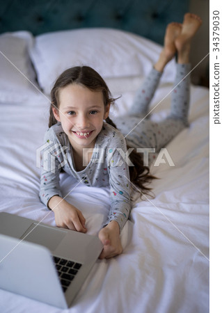 Smiling girl lying on bed with laptop in bedroom 34379030