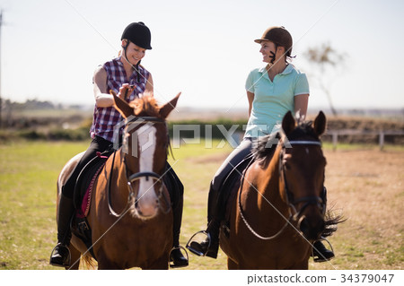 Full length happy female friends talking while horseback riding Full length happy female friends talking while horseback riding 34379047