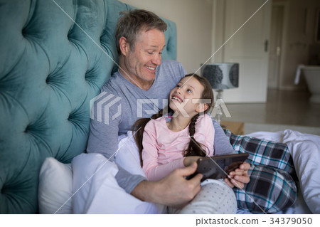 Smiling father and daughter using digital tablet on bed 34379050