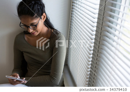 Woman using phone by window Woman using phone by window 34379410