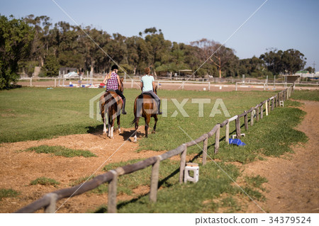 Female friends horseback riding at paddock 34379524