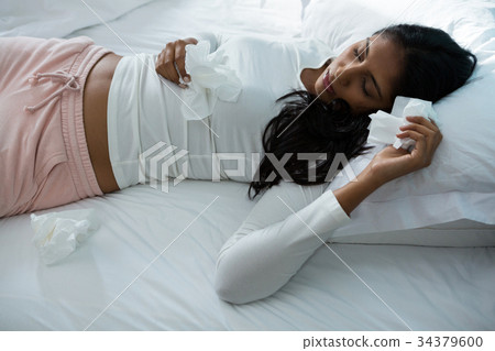 Sick woman holding tissue while sleeping on bed 34379600