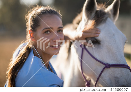 Portrait of smiling female vet checking horse Portrait of smiling female vet checking horse 34380007
