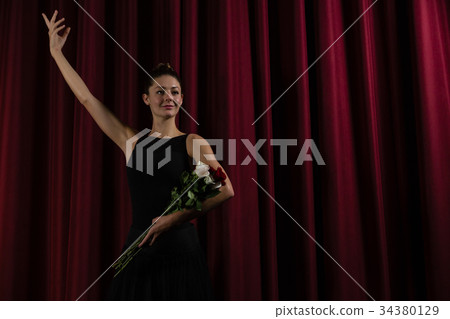 Ballerina posing with flower bouquet on stage Ballerina posing with flower bouquet on stage 34380129
