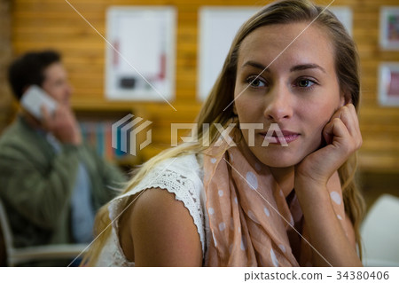 Thoughtful woman looking away while man talking on phone in background 34380406