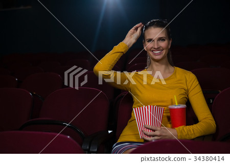 Woman having popcorn and drinks while watching movie in theatre 34380414