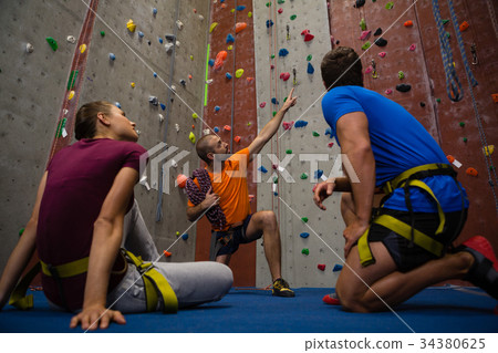Male trainer guiding athletes in wall climbing at gym 34380625