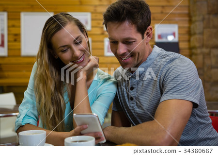 Couple using mobile phone while sitting at cafe 34380687