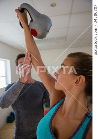 Trainer assisting female athlete in lifting kettlebells at club 34380707
