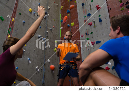 Low angle view of male trainer interacting with athletes sitting in gym 34380711