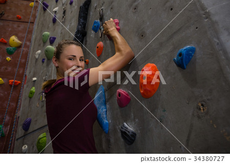 Portrait of confident female athlete climbing wall in gym 34380727