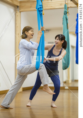 Trainer teaching aerial yoga to senior women 34385174