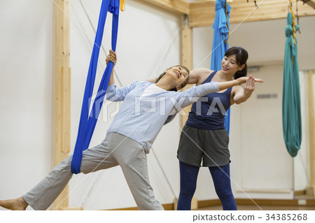 Female trainer teaching aerial yoga to senior women 34385268