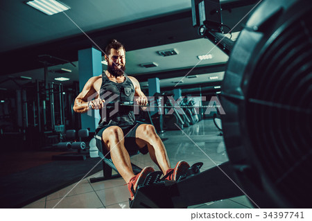 Muscular fit man using rowing machine at gym 34397741