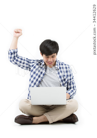 Casual happy Asian man using laptop on the floor Casual happy Asian man using laptop on the floor 34412629